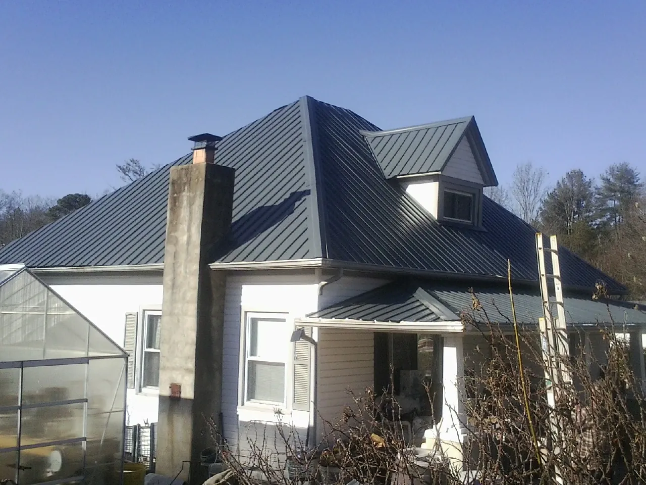 Dark blue standing seam metal roof on a white farmhouse with dormer — Slate & Tile Roof Repair by Roofing Brothers in Harris