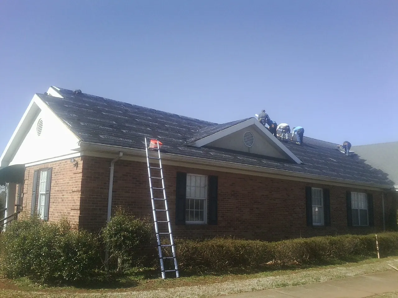 Crew tearing shingles off a brick ranch roof with a ladder set — Metal Roof Repair work by our crew in Harris