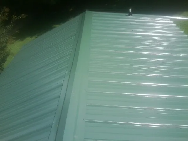 New green metal panels meeting at the ridge of a roof — Flat Roof Repair work by our crew in Harris