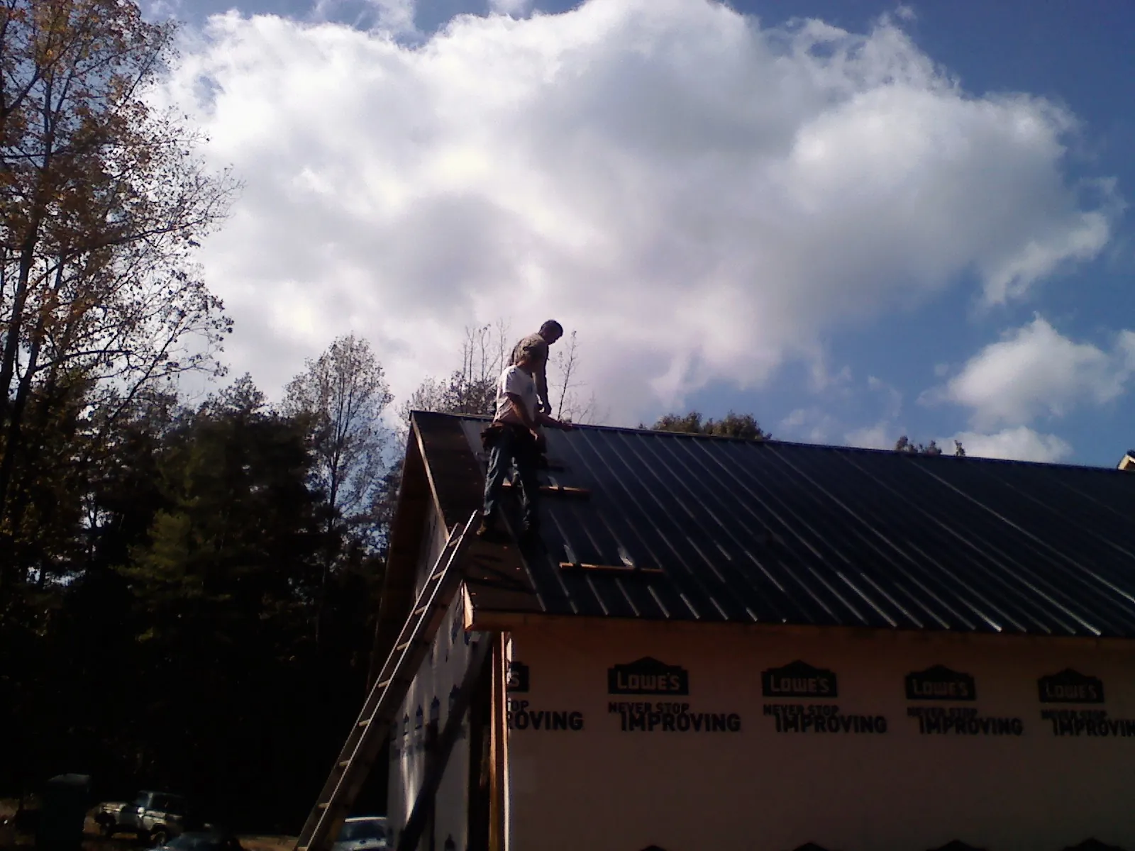 Roofer fastening dark metal panels high against a cloudy sky, from a Roof Inspection job in Harris