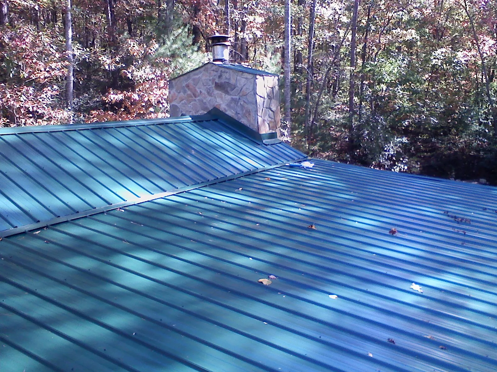 New green metal roof and stone chimney surrounded by autumn woods in Harris